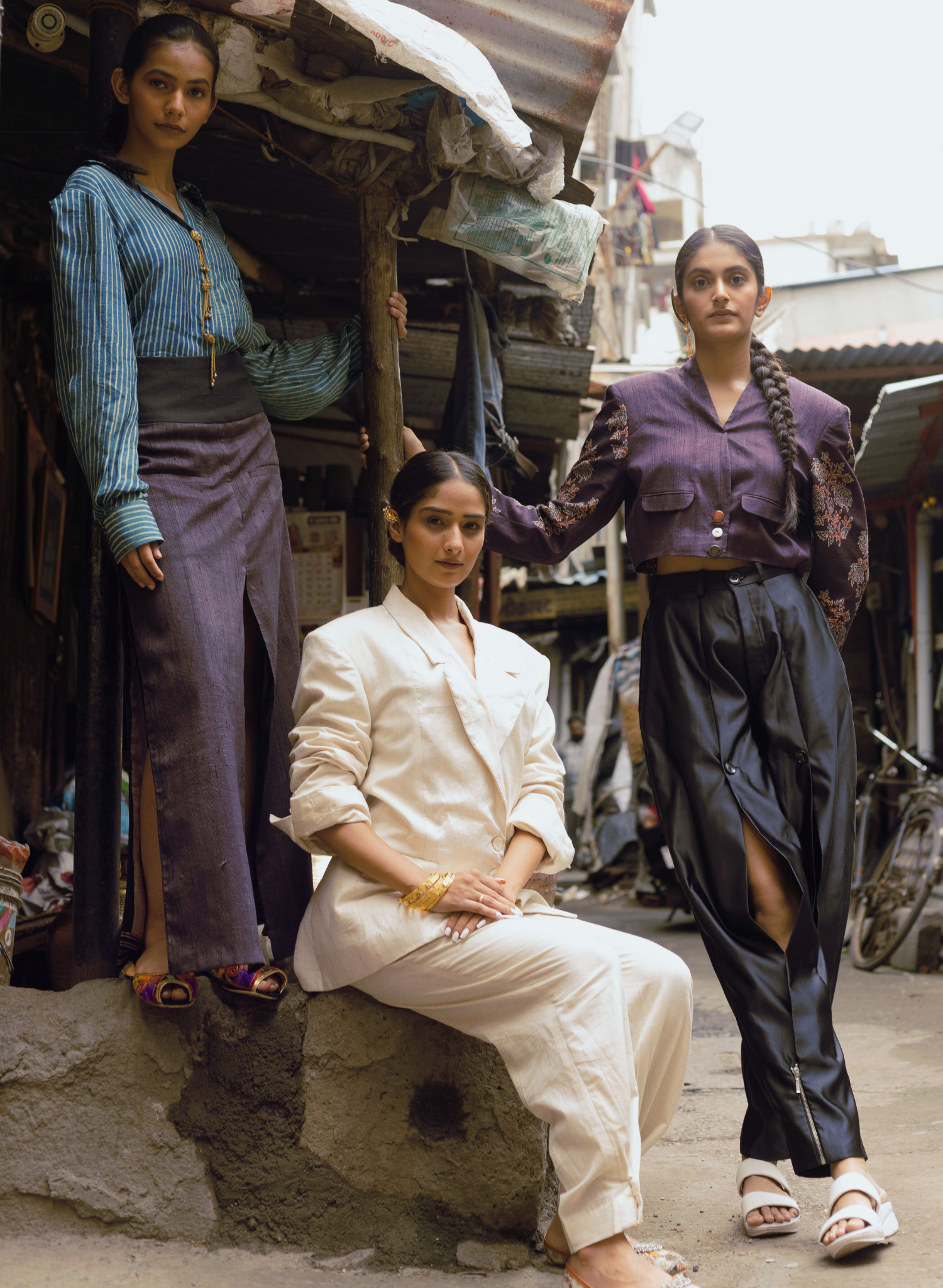 Three models showcasing Indian handcrafted high-fashion pieces with a modern streetwear twist, featuring Ajrakh print handloom jacket, shirt, skirt set, and vintage-inspired shoes.